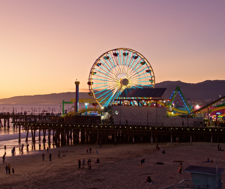 Aerial view of the Santa Monica Pier with a ferris wheel lit up and the sun setting behind it