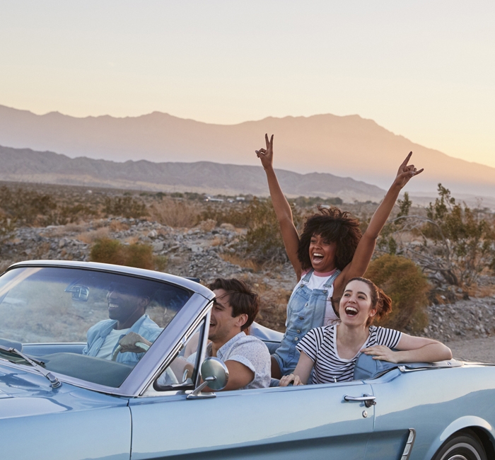 a group of friends driving in a car while someone in the back holds up peace signs