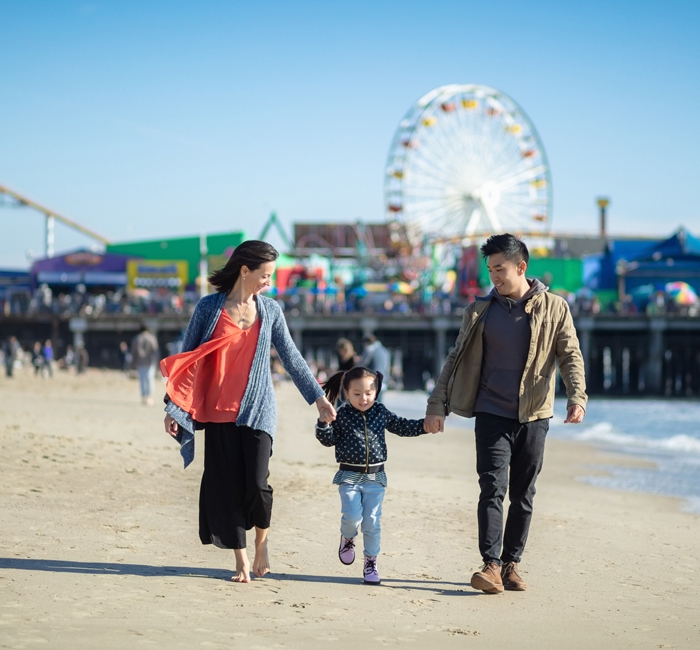 A family walking on the beach with the Santa Monica Pier in the background