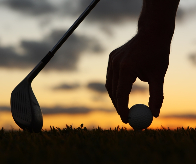 someone setting up a golf ball on a tee with the sun setting in the background